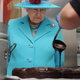 Queen Elizabeth watches as a person pours chocolate sauce out of a ladle